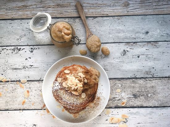 Pancakes-Stapel auf einem weissen Teller mit Mandelblättchen, daneben Obstkompott, alles auf einem weiß gekalkten Holztisch