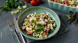 Erdbeer Tabouleh aufgrünem Kermaikteller mit Besteck links und Zutaten im Hintergrund