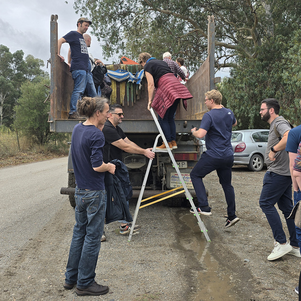 KI generiert: Eine Gruppe von Menschen klettert mit Hilfe einer Leiter auf die Ladefläche eines LKWs. Die Szene scheint in einer ländlichen Umgebung stattzufinden.