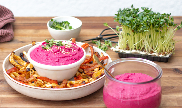 KI generiert: Schale mit pinkem Dip, Gemüsechips und Sprossen auf einem Holztisch.