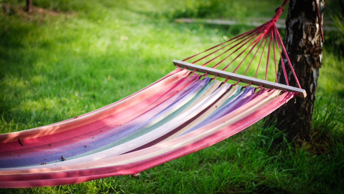 KI generiert: Eine bunte Hängematte hängt zwischen Bäumen auf einem grünen Rasen.