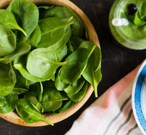 frischer Blattspinat in Holzschüssel neben einem Green Smoothie