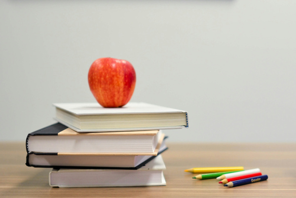 KI generiert: Ein roter Apfel auf einem Bücherstapel, daneben liegen bunte Stifte.