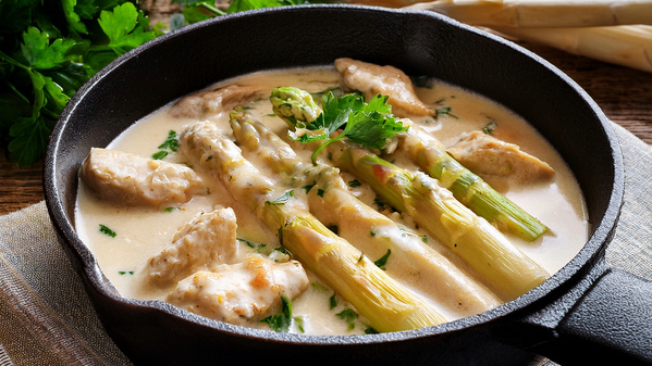 KI generiert: Eine Pfanne mit Spargel und Fleisch in einer cremigen Sauce, dekoriert mit Petersilie.