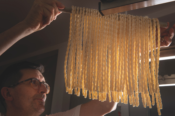 KI generiert: Person hält frisch zubereitete Pasta, die zum Trocknen aufgehängt wird.