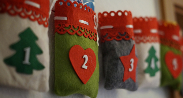Das Bild zeigt einen Adventskalender mit dekorativen Säckchen aus Filz, die nummeriert sind. Die Säckchen sind mit Motiven wie Bäumen, Herzen und Sternen verziert.