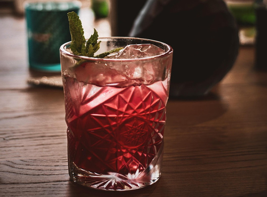 KI generiert: Ein Glas mit rotem Getränk und Minze auf einem Holztisch.