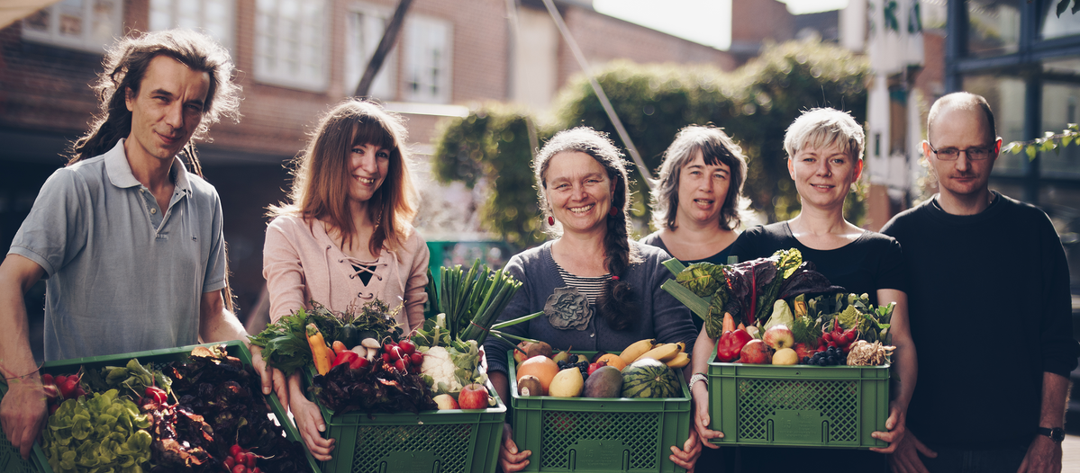Grünland Bioladen und Lieferdienst Team mit Biokisten voll Obst und Gemüse im Arm
