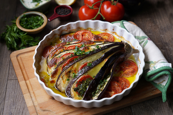 KI generiert: Gebratene Aubergine und Tomaten in einer runden Ofenform auf einem Holzbrett.