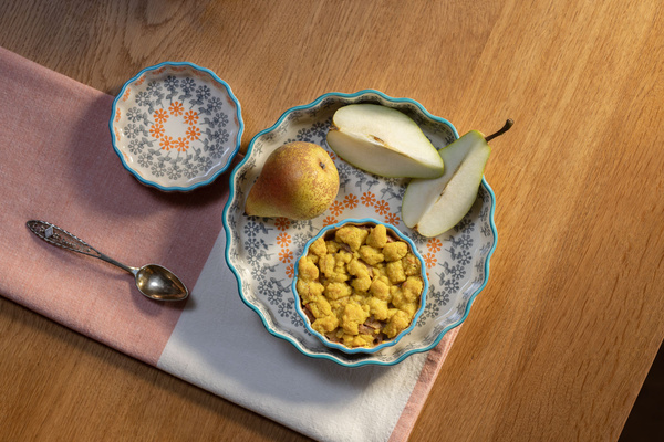 KI generiert: Eine Schale mit einer Birne, Birnenspalten und Cereal auf einem Tisch mit Löffel und Serviette.