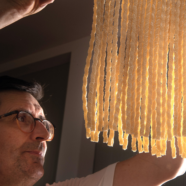 KI generiert: Eine Person betrachtet hängende getrocknete Nudeln in warmem Licht.