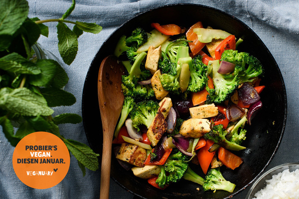 KI generiert: Das Bild zeigt eine Pfanne mit einer Vielzahl von gebratenem Gemüse und Tofu, umgeben von frischen Kräutern. In der Ecke befindet sich ein Hinweis auf eine vegane Aktion im Januar.