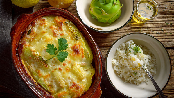  Ein Kohlrabi-Gratin in einer Auflaufform, daneben Reis, ein grünes Gemüse und ein Glas Öl.
