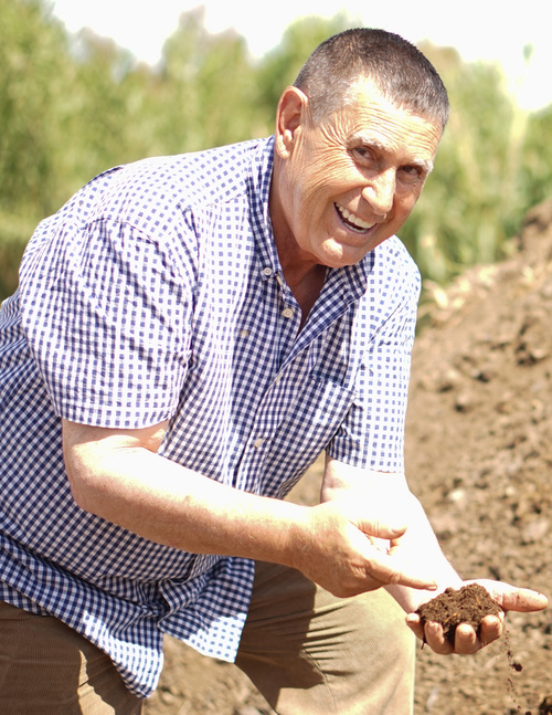KI generiert: Ein Mann begutachtet lächelnd Erde im Freien.