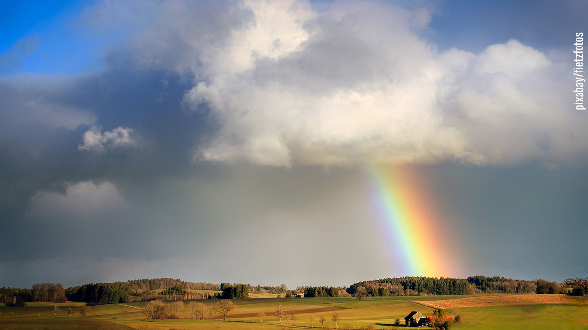 Leicht hügelige Landschaft mit Wolkenhimmel und Regenbogen