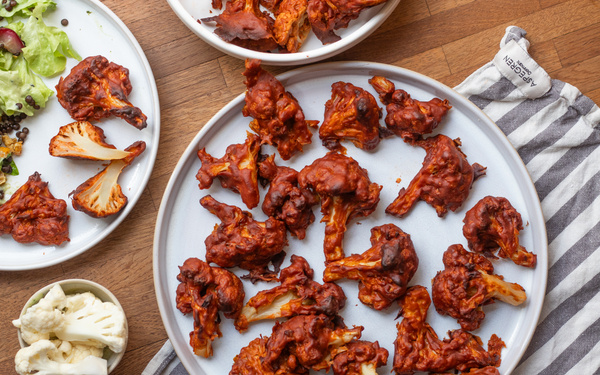KI generiert: Gebackener Blumenkohl in Barbecue-Soße auf Tellern, mit etwas Salat und rohem Blumenkohl als Beilage.