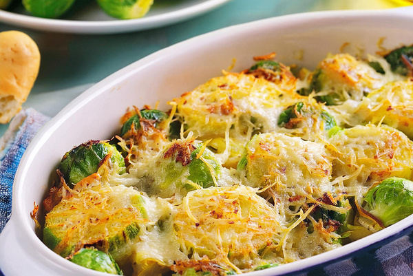 In einer ovalen Auflaufform ist der Rosenkohl mit Kartoffelkruste gebacken worden. Unter der blauen Auflaufform liegt ein blau-weiß-kariertes Tuch.