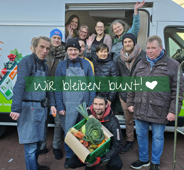 KI generiert: Gruppe von Menschen vor einem Lieferwagen, jemand hält eine Gemüsekiste.  
Text: "wir bleiben bunt! ♥"