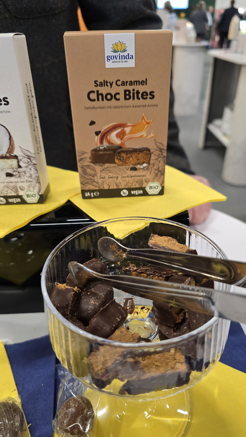 KI generiert: Glas mit Schokoladenstücken, Verpackung: "govinda Salty Caramel Choc Bites".
