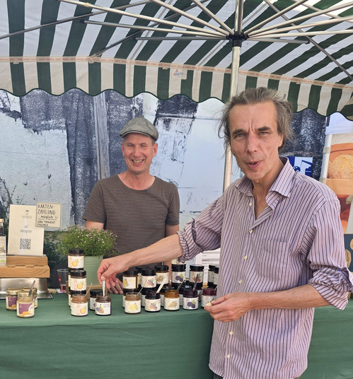 KI generiert: Zwei Männer an einem Marktstand mit Marmeladengläsern. Text: "KARTENZAHLUNG möglich, FOLGT DEM KREIDEPFEIL!"