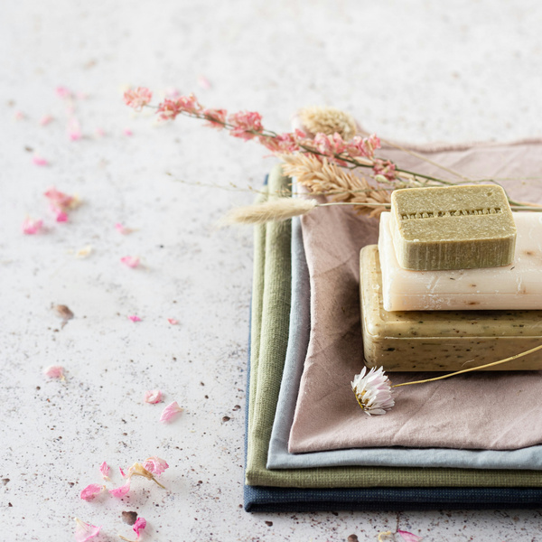 KI generiert: Drei Naturseifen auf gestapelten Stoffen mit getrockneten Blumen dekoriert.