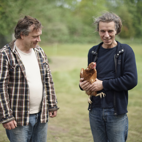 KI generiert: Zwei Männer stehen im Freien, einer hält ein Huhn in den Armen.