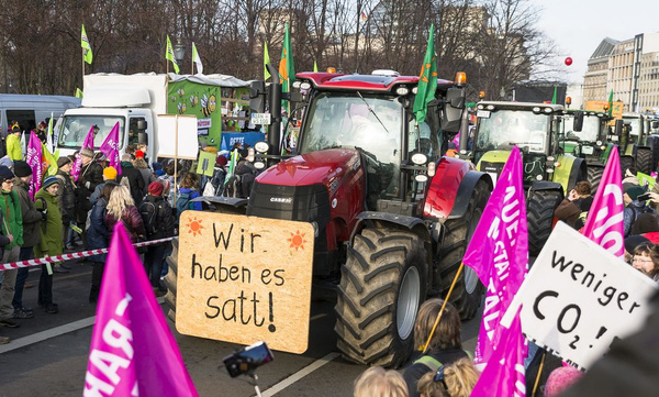 KI generiert: Menschen demonstrieren neben Traktoren mit Plakaten. Text: "Wir haben es satt!", "weniger CO₂!".