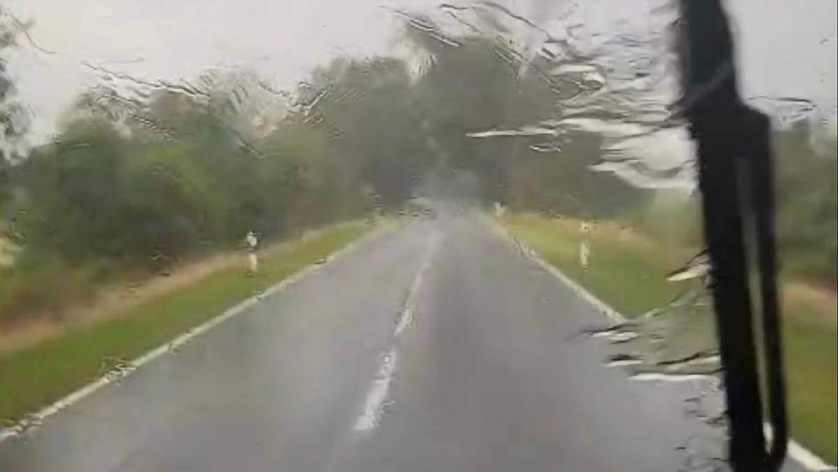 KI generiert: Eine verregnete Straße, gesehen durch eine Windschutzscheibe mit Wischer.