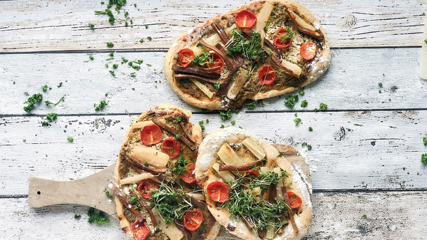 KI generiert: Fladenbrote mit Kräutern, Tomaten und Spargel auf einem Holzbrett.