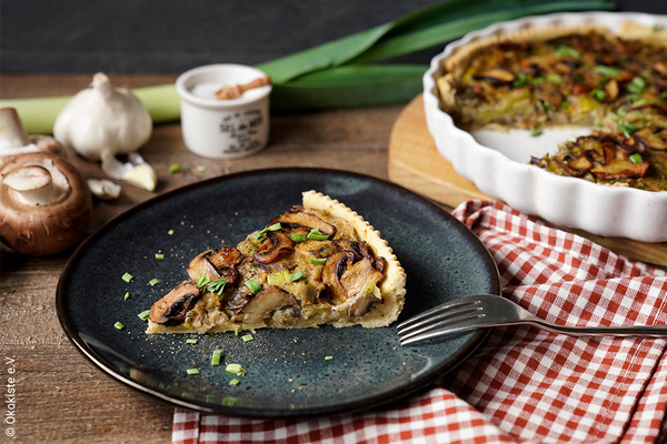 KI generiert: Ein Stück Pilzquiche auf einem Teller, umgeben von frischen Zutaten.