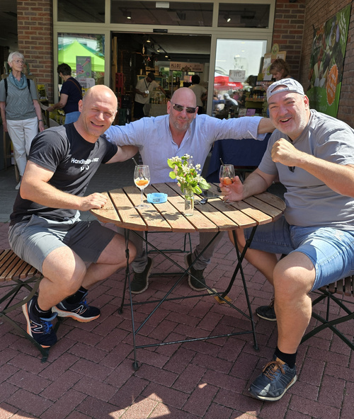 KI generiert: Drei Personen sitzen an einem Tisch im Freien und genießen Getränke.