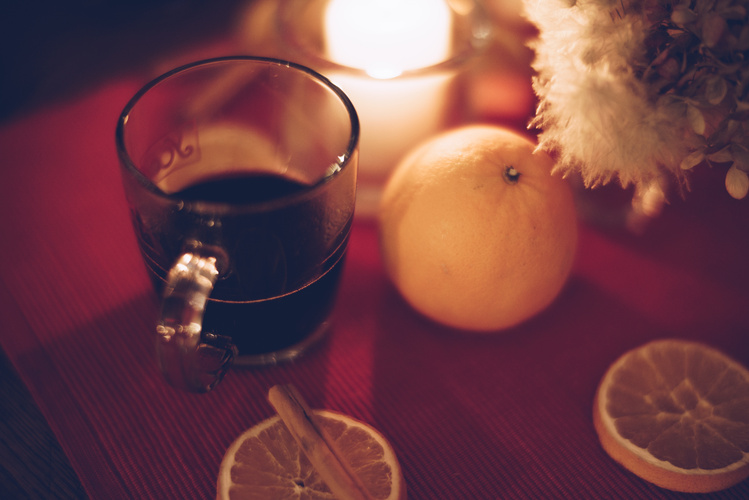 KI generiert: Ein Glas mit heißem Getränk, Orange, Kerze und getrocknete Blumen auf einem roten Untergrund.