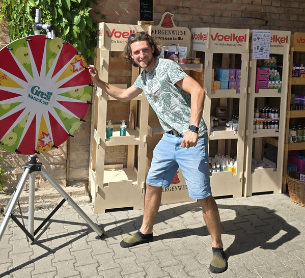 KI generiert: Ein Mann dreht ein Glücksrad vor einem Naturkostladen mit Produkten und Werbung.