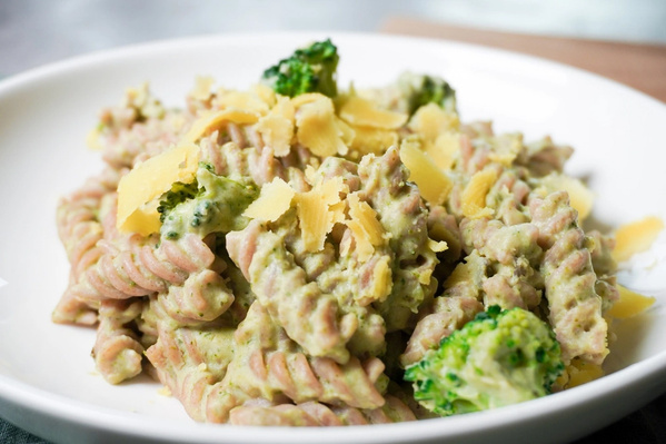 KI generiert: Eine cremige Pasta mit Brokkoli und Käsestreifen auf einem weißen Teller.