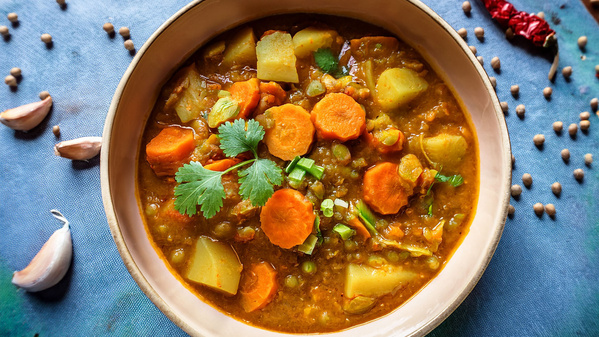 Ein Teller mit gemischtem Gemüse-Curry, garniert mit Korianderblättern, umgeben von Linsen, Knoblauch und Chili.