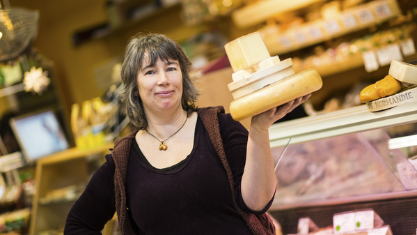 Bioladen-Mitarbeiterin präsentiert Käsestapel, im Hintergrund Käsetresen