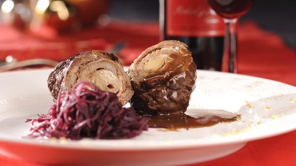 KI generiert: Ein Teller mit Rinderroulade und Rotkohl, im Hintergrund eine Weinflasche und Glas.