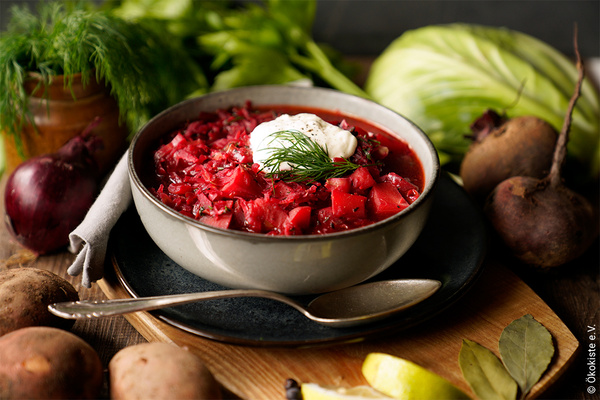 KI generiert: Eine Schüssel Borschtsch mit Sauerrahm, umgeben von frischen Zutaten. Text: "Ökokiste e.V."