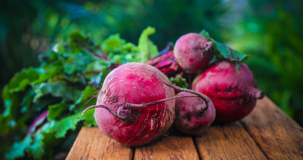KI generiert: Frische Rote Beete auf einem Holztisch, im Hintergrund grünes Laub.