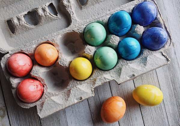 KI generiert: Bunte, gefärbte Eier in einem Eierkarton auf hellem Holzhintergrund.