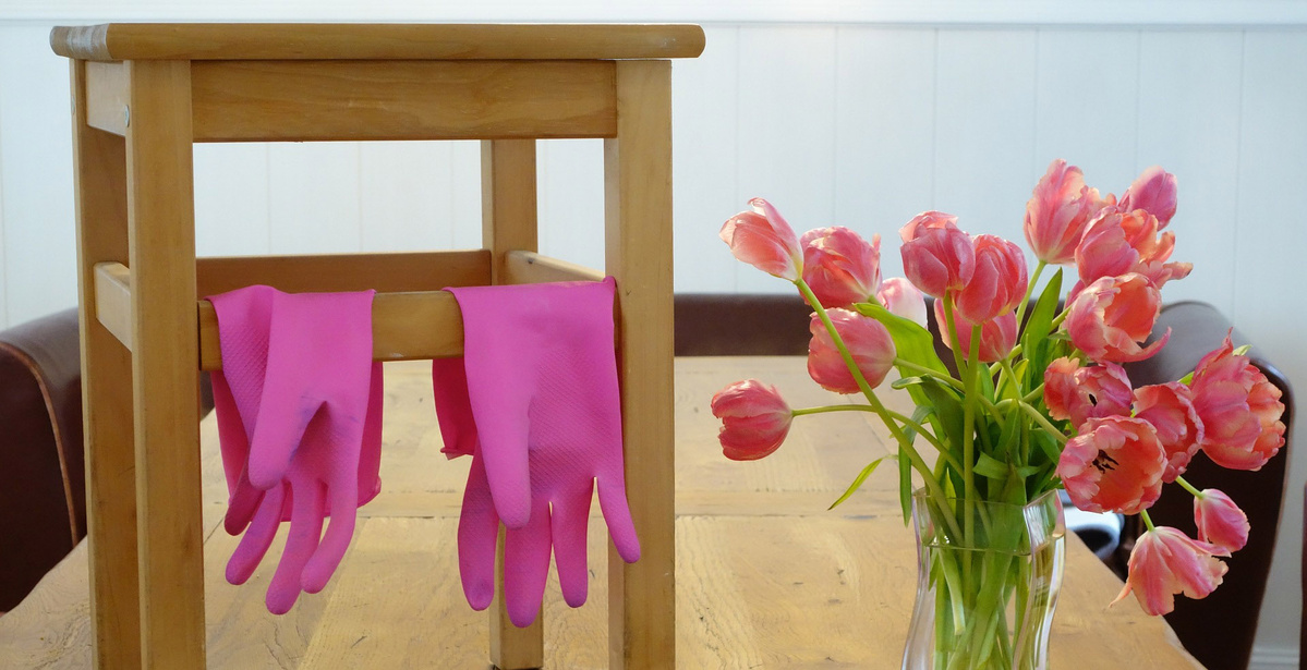 Pinke Putzhandschuhe auf Holzstuhl neben rosa Tulpenstrauss