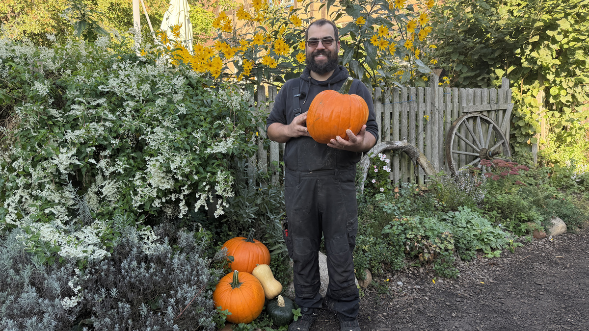 Aram Quis hält einen Halloween-Kürbis in der Hand und hat weitere Kürbisse zu seinen Füßen