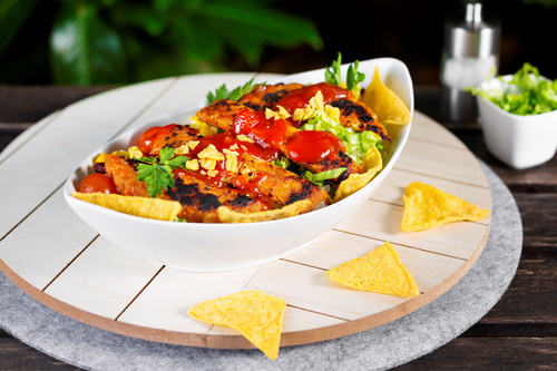 KI generiert: Eine Schale mit buntem Salat, Nachos und roter Sauce, angerichtet auf einem runden Brett.