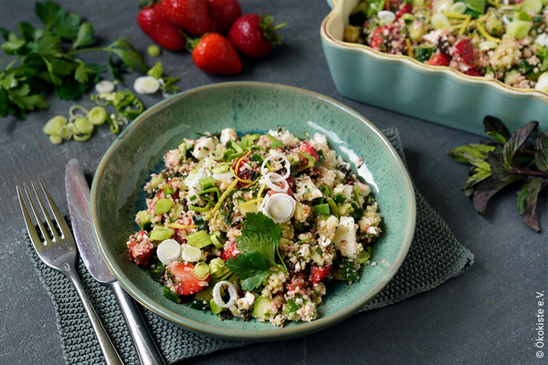 Ein bunter Couscous-Salat mit Erdbeeren, frischen Kräutern und Gemüse in einer Schüssel, umgeben von Zutaten.