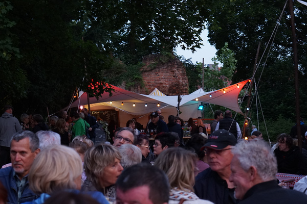 KI generiert: Ein geselliges Open-Air-Event mit vielen Menschen vor einem beleuchteten Zelt.