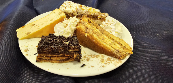 KI generiert: Das Bild zeigt einen Teller mit verschiedenen Kuchensorten, umgeben von Sahne. Die Speisen liegen auf einem dunkelblauen Tuch.