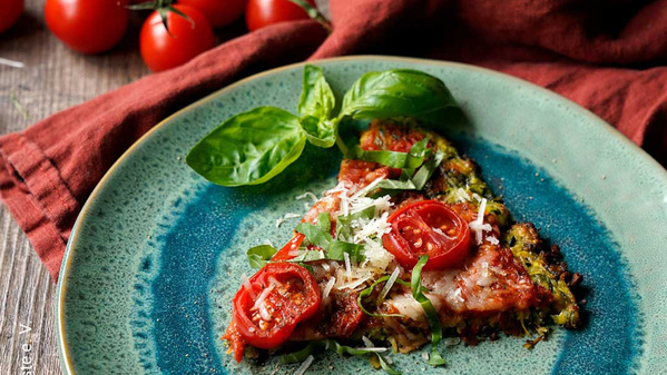 Pizza-Slice mit Tomaten, Basilikum und Käse auf einem grünen Teller, dekoriert mit frischem Basilikum.