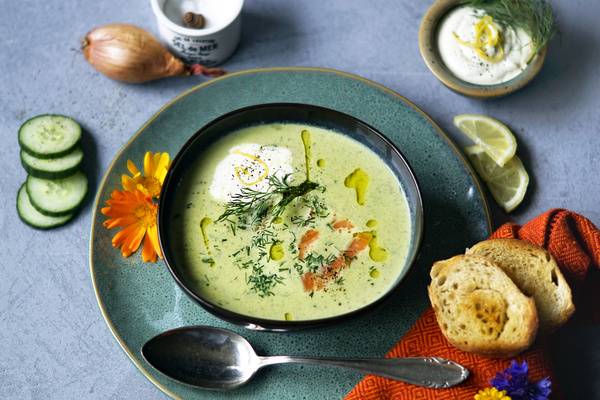 KI generiert: Ein Teller mit cremiger Kräutersuppe, dekoriert mit Dill, Sahne und Lachs, umgeben von Brot und frischen Beilagen.