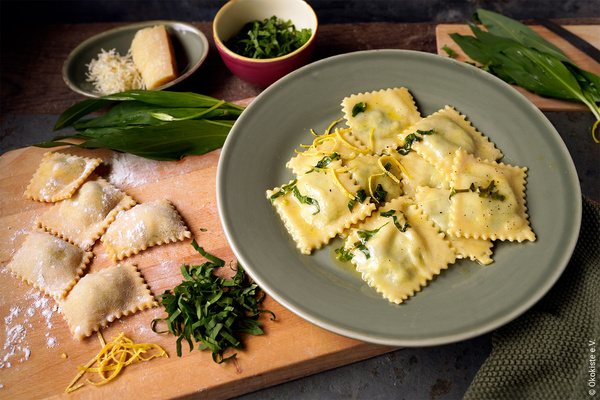 KI generiert: Ravioli mit Kräutern und Zitrone; daneben frische Zutaten auf einem Schneidebrett.