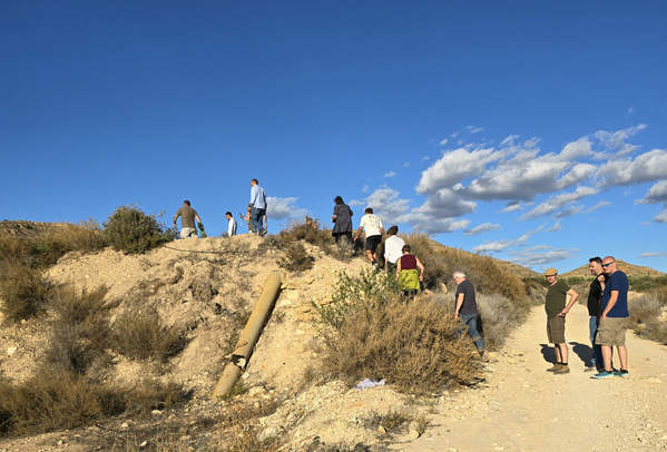 KI generiert: Das Bild zeigt mehrere Personen, die einen Hügel in einer trockenen Landschaft hinaufgehen. Der Himmel ist klar mit wenigen Wolken.